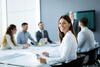 a smiling woman holding a document looks over from her table of coworkers